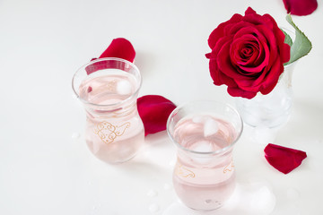 Two cup Refreshing Rose water lemonade with ice cubes and Rose flower in glass and petals on white background. Selective focus.