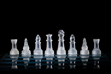 Glass Chess Set Standing on a Chessboard with a Dark Background, including the Rook, Knight, Bishop, Queen and King Pieces