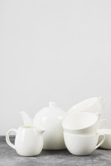 Fototapeta na wymiar Clean white tableware (teapot, cups, saucers) on a gray background