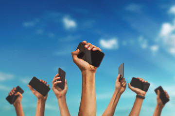 group of people's hands holding phones and rising them up against sky