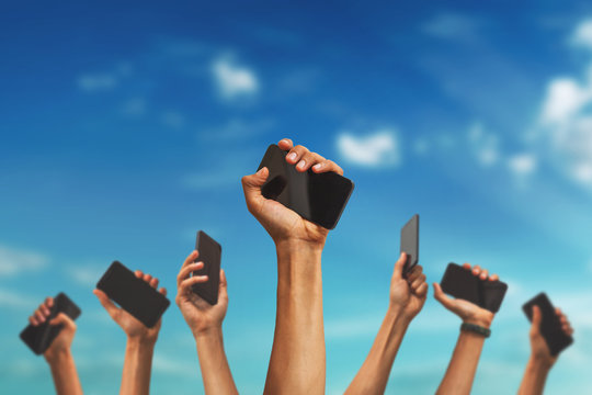 Group Of People's Hands Holding Phones And Rising Them Up Against Sky