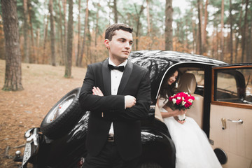Beautiful wedding couple posing near splendid retro car
