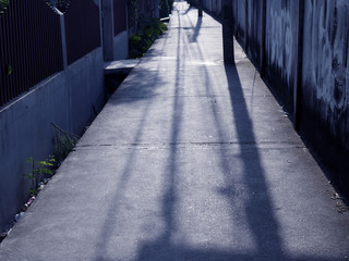 Old narrow village cement pathway alley between both side house walls, with cool evening sunlight shade and electrical pole with power cord shadow background 