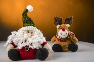 Pupazzi simpatici di babbo Natale e renna su superficie bianca riflettente - sfondo colore senape