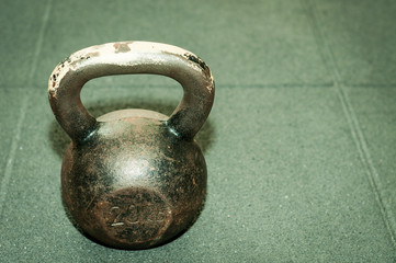 Fototapeta na wymiar Old heavy rusty kettlebell weight on the black gym floor with selective focus and film grain
