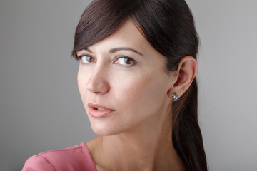 Closeup portrait of beautiful surprised young brunette Caucasian woman with brown eyes looking in camera. Girl female with long dark hair in pink shirt clothes. Studio beauty shot.