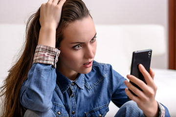 Young woman holding his head and looks to the smartphone. Distressed by what he saw