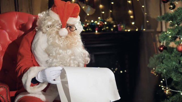Happy Santa eading the gift list at fireplace during christmas eve. 4K.