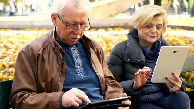 Mature couple using tablet computer sitting on a bench in the city park
