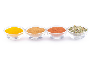Ground red pepper, paprika, turmeric and italian herbs in glass bowls isolated on white background