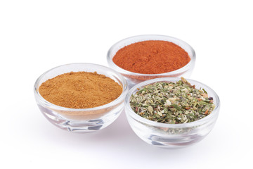 Ground red pepper, paprika and italian herbs in glass bowls isolated on white background