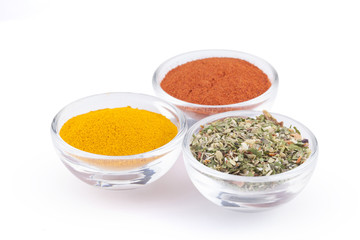 Ground turmeric, paprika and italian herbs in glass bowls isolated on white background