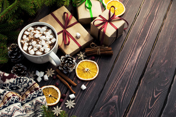 A cup of hot coffee with marshmallow, spruce branches, cones, Christmas gifts, mugs of orange, snowflakes, cinnamon. Traditional festive decoration Christmas dark background top view.