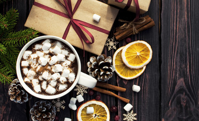 Fototapeta na wymiar A cup of hot coffee with marshmallow, spruce branches, cones, Christmas gifts, mugs of orange, snowflakes, cinnamon. Traditional festive decoration Christmas dark background top view.