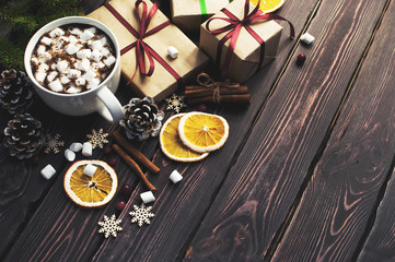 A cup of hot coffee with marshmallow, spruce branches, cones, Christmas gifts, mugs of orange, snowflakes, cinnamon. Traditional festive decoration Christmas dark background top view.