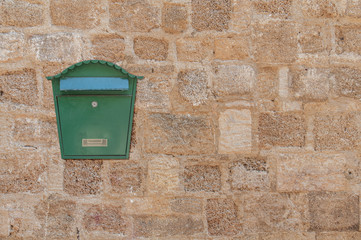 Green metal mail box hanging on left side of yellow concrete house wall
