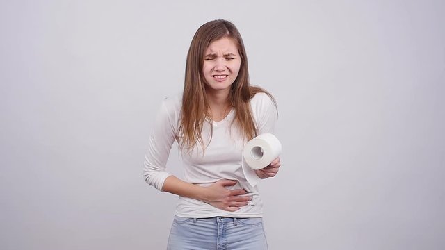 Young woman suffering from stomach ache on a gray background
