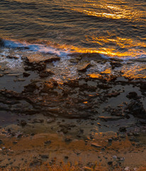 Breaking waves on rocky seashore and sun reflections at sunset