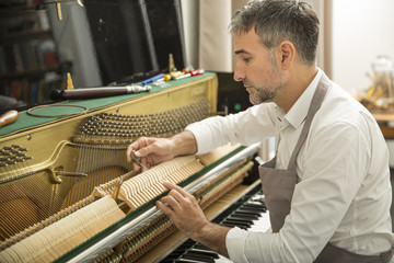 Technician tuning a upright piano using lever and tools © Atelier 211