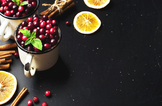 Fresh red cranberries with mint leaves in a white cup, cinnamon on a dark black background with copy space top view.