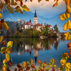 Bled, Slovenia - Beautiful autumn sunrise at Lake Bled with the famous Pilgrimage Church of the Assumption of Maria with Bled Castle and Julian Alps at background. Framed with autumn foliage
