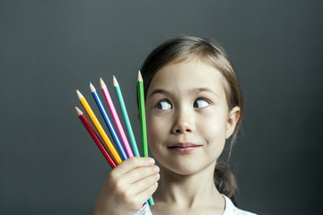 Little artist slyly looks at colored pencils: she has a new creative idea for painting