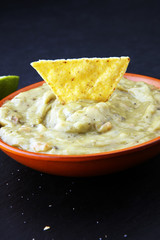 Bowl of guacamole with tortilla chips on dark background.