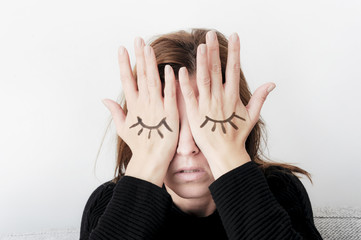 Young woman is covering her eyes with her palms. Eyes painted on her hand. Sorrow concept.