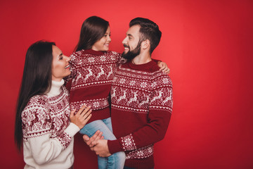 Three relatives bonding, married couple of brunet and brunette, excited small girl, in knitted cute traditional costumes, jeans, embracing, holly molly noel x mas time!
