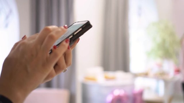 The woman with red manicure writes messages in the smartphone. The young woman holds the smartphone in hand. typing text on touch screen