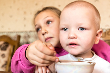 The elder sister takes care of a little brother and treats with tea and rolls. Selective focus.