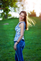 Fototapeta premium Gorgeous girl in blue jeans and a T-shirt, walks in the park at sunset background