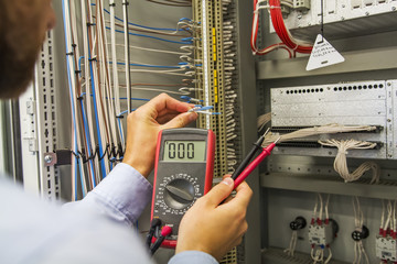 Electrician engineer with multimeter tests electrical control panel of automation equipment....