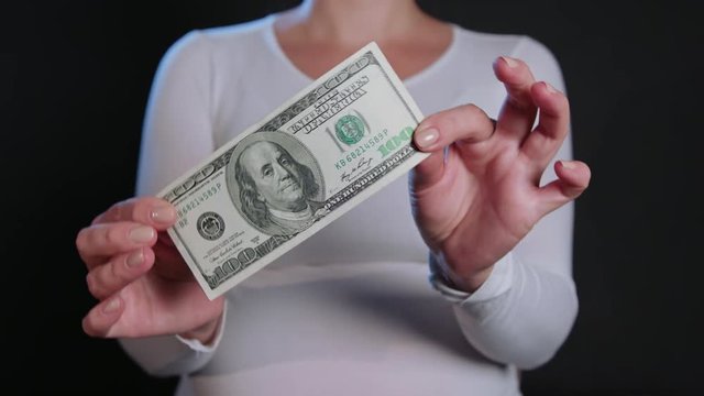 A woman in a white sweater holding cash (US Dollar banknotes) against a black background. Close-up shot