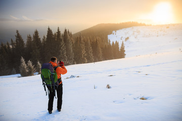 Fototapeta na wymiar Hiker in winter mountains. Young man has a rest in mountains. Man with backpack trekking in mountains. Winter hiking. Beautiful sunrise in the winter mountains