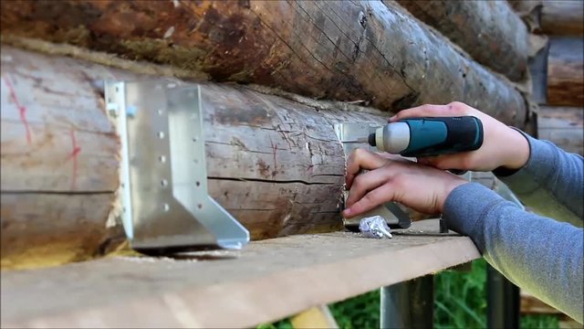 Assembling a wooden frame and building a house. Russia. The worker fixes fastenings for floor construction in a wooden house, drills screw holes with a drill tool.