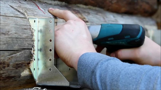 Assembling a wooden frame and building a house. Russia. The worker screw the screws into the pre-drilled holes with a screwdriver.