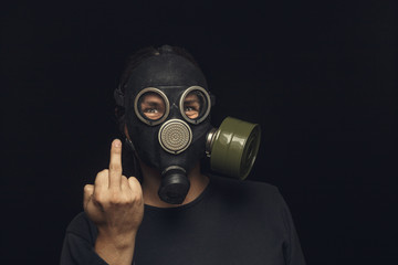 Portrait of man in gas mask on dark background, shows middle fingers sign by one hands