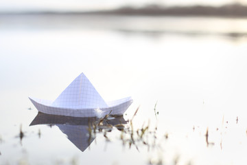 Origami paper ship sailing in river. Paper boat made from mathematics notebook paper.