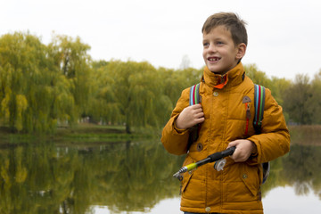 Side view on boy in yellow jacket using fishing rod outdoors at pond during cool autumn day