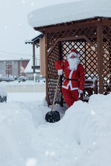 Proud santa claus lean on shovel after work of snow removal in front of wooden house