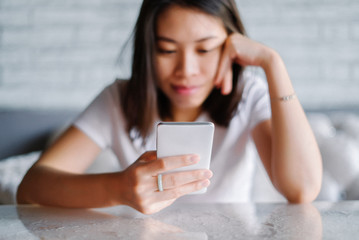 Relaxed asian woman use smart phone reading text message on white sofa.