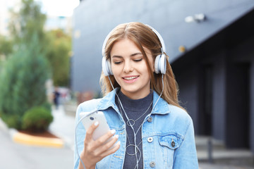 Beautiful young woman with mobile phone listening to music outdoors