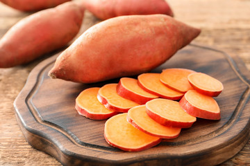 Board with raw sweet potatoes on wooden table