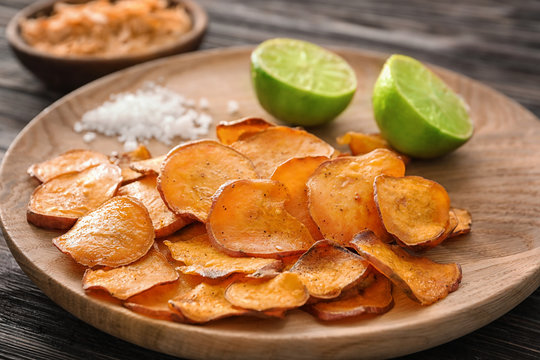 Plate with yummy sweet potato chips on wooden table