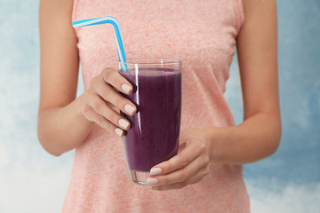 Woman holding glass with purple smoothie on light background