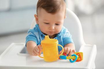 Cute baby with bottle of water sitting at table indoors