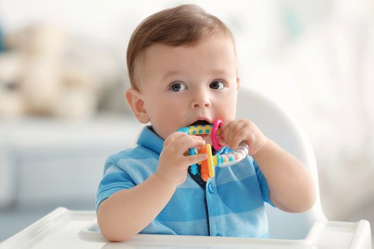 Cute baby with rattle sitting on chair indoors