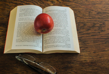 red apple resting on the book with glasses on the table
