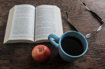 book on the table with coffee, apple and eyeglasses